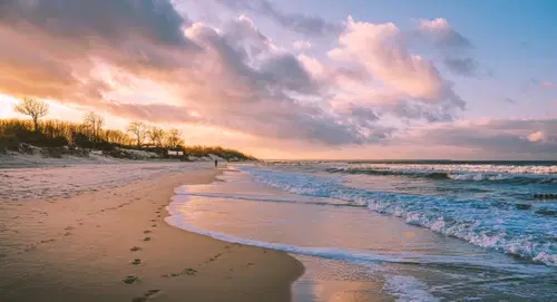 Ein sch&ouml;ner Strand bei Sonnenuntergang mit sanften Wellen, footprints im Sand und einem bew&ouml;lkten Himmel.