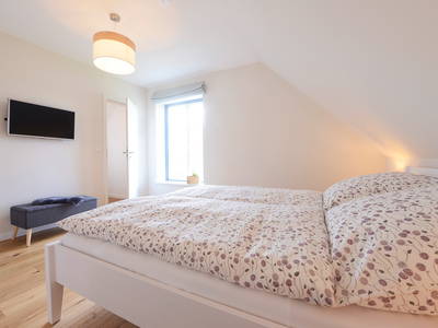 Blick ins Schlafzimmer mit Doppelbett, TV und begehbarem Kleiderschrank